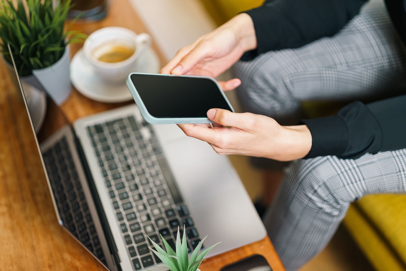 Business owner testing a mobile app on a smartphone beside a laptop before launch